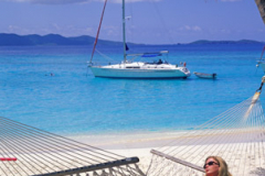 Woman relaxing in a hammock on beach with moored yacht  at White Bay Jost Van Dyke British Virgin Islands