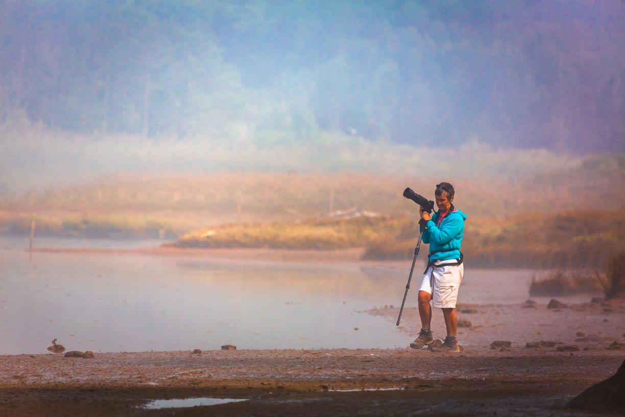 Female photographer carrying camera and monopod on the edge of a misty Óbidos lagoon